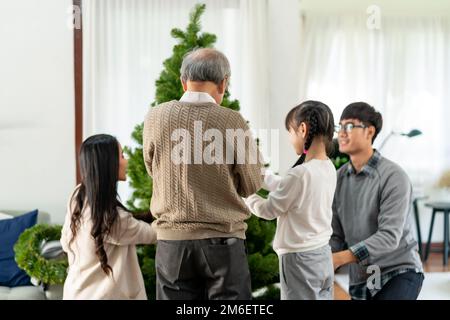 Eine Mehrgenerationsfamilie, die einen Weihnachtsbaum als Weihnachtsgruß schmückt. Stockfoto