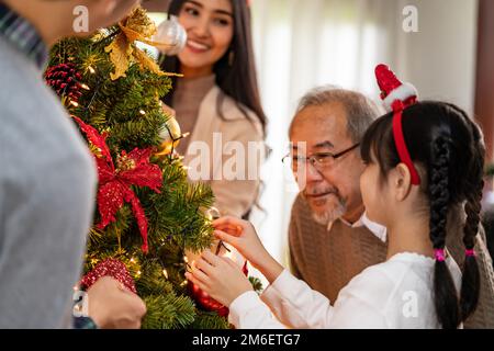 Eine Mehrgenerationsfamilie, die einen Weihnachtsbaum als Weihnachtsgruß schmückt. Stockfoto