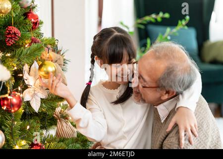 Mädchen und Großvater schmücken einen Weihnachtsbaum als Weihnachtsgruß. Stockfoto