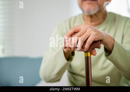 Die Hände eines alten Asiaten, der zu Hause ruht, halten einen hölzernen Gehstock Stockfoto