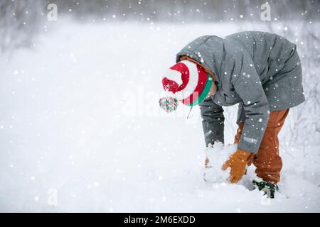 Ein Junge macht einen Schneeball auf einem verschneiten Feld. Ein Kind spielt im Winter mit Schnee. Stockfoto