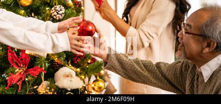 Ein älterer Mann schmückt den weihnachtsbaum mit seiner Familie. Stockfoto