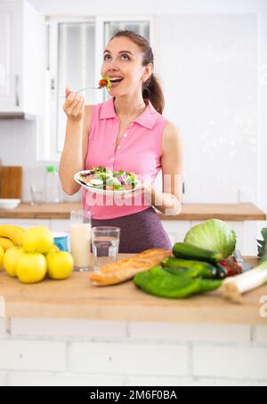 Schlanke junge Frau, die Gemüsesalat in der Küche isst Stockfoto