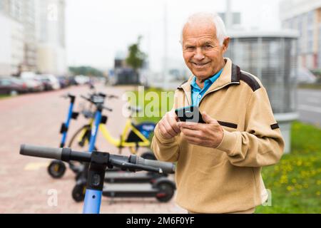 Großvater will einen Elektroroller fahren und zahlt Miete mit Handy Stockfoto