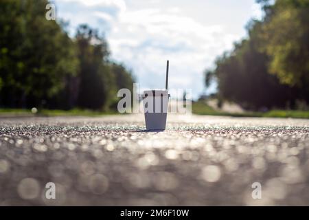 Ein weißer Pappbecher mit Deckel und einer Röhre steht auf der Straße in die Stadt. Stockfoto