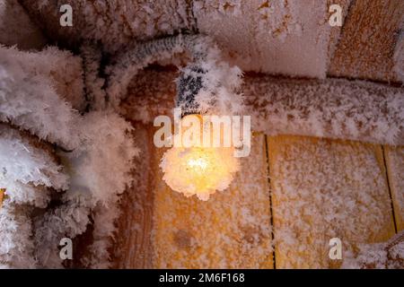 Schneekristalle an einer Holzwand und eine Glühbirne. Stockfoto