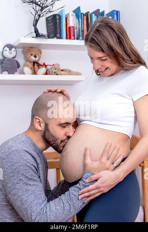 Ein glücklicher, erwartender Vater, mit dem Kopf auf dem Bauch seiner Frau, der sein ungeborenes Kind küsst. Reizende zukünftige Eltern. Stockfoto