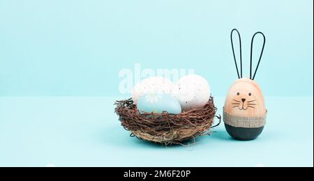 Osterhasen oder Kaninchen, die in einem Weidennest voller bunter Eier sitzen, Frühlingsferien Stockfoto