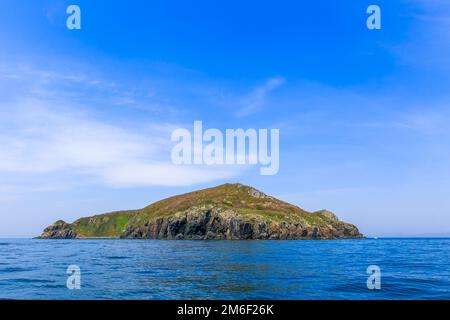 Eine kleine unbewohnte grüne Insel inmitten eines ruhigen blauen Meeres und blauen Himmels. Schöner Entspannungshintergrund. Stockfoto