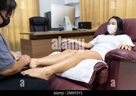 Neue normale asiatische Frau mit Gesichtsmaske tun Massage zu Hause Stockfoto