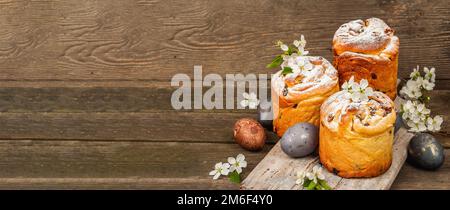Osterkuchen Cruffin oder süßes Brot kulich mit bemalten Eiern. Traditionelles festliches Backen und frische Kirschblumen, festlicher Holzhintergrund. Jahrgang b Stockfoto