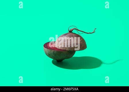 In Stücke geschnittener Rote-Bete-Minimalist auf einem grünen Tisch. Rote Rüben in zwei Hälften geschnitten, isoliert auf einem bunten Hintergrund. Stockfoto