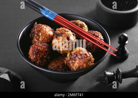 Chinesische oder indische Veg Manchurian in einer schwarzen Schüssel mit Essstäbchen - Asiatische Küche Stockfoto