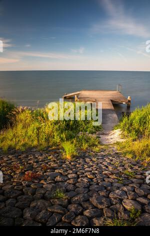 Holzsteg an der Seeküste im abendlichen Sonnenlicht mit blauem Himmel lange Exposition Stockfoto