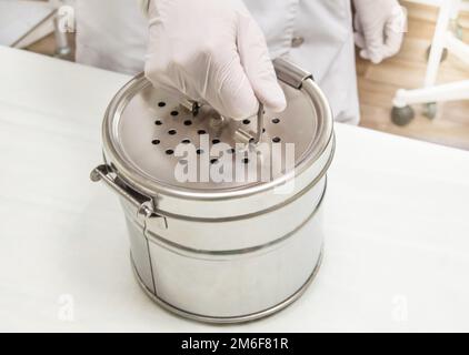 Runder Edelstahlsterilisator in den Händen einer Krankenschwester in Gummihandschuhen. Vorbereitung zur Autoklavsterilisation Stockfoto