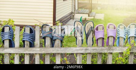 Sommerschuhe Flip-Flops für eine fröhliche, freundliche Familie hängen an einem sonnigen Sommertag draußen an einem Holzzaun Stockfoto