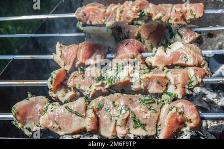 Nahaufnahme von mariniertem Fleisch, das auf einem Metallspieß im Freien geröstet wurde, an einem Sommertag, der Rauch aus den Kohlen, das Konzept eines Fotos Stockfoto