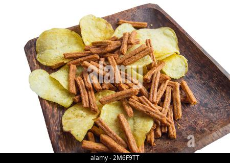Köstliche Kartoffelchips und gesalzene Roggenbrot-Cracker auf einer dunklen Holzplatte, isoliert auf weißem Hintergrund durch Schneiden Stockfoto