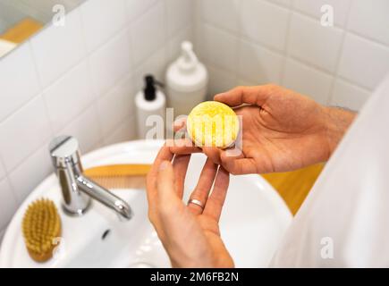 Ein Mann im Badezimmer mit einem soliden Shampoo-Riegel. Plastikfrei, kein Abfall, geringe Wassermenge. Nachhaltige Haarpflege. Verantwortung wählen Stockfoto