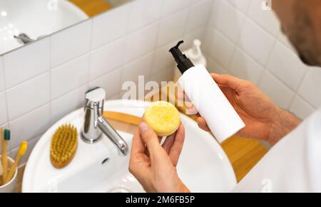 Der Mann hat die Wahl zwischen einem festen Shampoo-Riegel und einem flüssigen. Plastikfrei, kein Abfall, geringe Wassermenge. Nachhaltige Haarpflege. Badezimmer Stockfoto