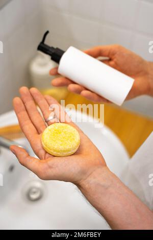 Der Mann hat die Wahl zwischen einem festen Shampoo-Riegel und einem flüssigen. Badezimmerzubehör. Nachhaltige Haarpflege. Ohne Plastik, ohne Abfall, wenig Abfall Stockfoto