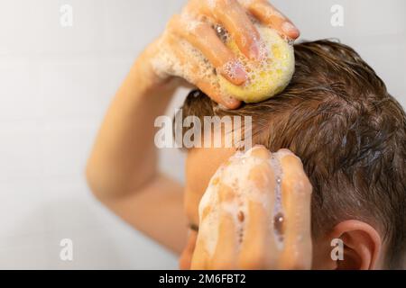 Ein Mann benutzt eine solide Shampoo-Bar im Bad. Nachhaltige Haarpflege. Shampoo auf die Kopfhaut auftragen. Ohne Plastik, ohne Abfall, wenig Wasser Stockfoto