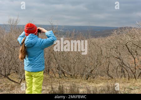 Ein Mädchen an einem Herbsttag schaut durch ein Fernglas vom Berg, Rückansicht Stockfoto