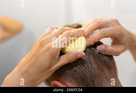 Ein Mann trägt einen soliden Shampoo-Stab auf das Haar auf. Nachhaltige Haarpflege. Mann im Badezimmer. Plastikfrei, kein Abfall, geringe Wassermenge. Stockfoto
