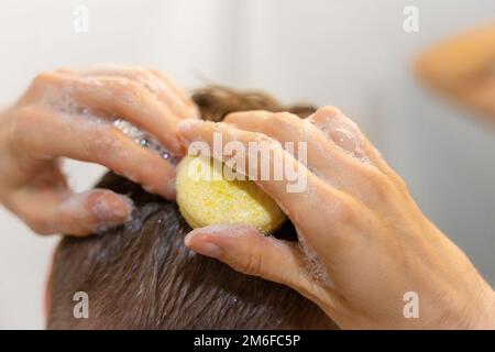 Ein Mann benutzt eine solide Shampoo-Bar im Bad. Shampoo auf die Kopfhaut auftragen. Nachhaltige Haarpflege. Ohne Plastik, ohne Abfall, wenig Wasser Stockfoto