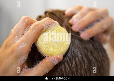 Ein Mann trägt einen soliden Shampoo-Stab auf das Haar auf. Mann im Badezimmer. Nachhaltige Haarpflege, umweltfreundliche Kosmetik. Ohne Plastik, ohne Verschwendung Stockfoto