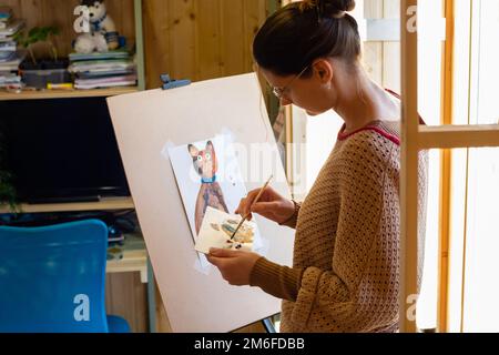 Der Künstler mischt zu Hause Farben auf einem Palettengemälde Am Fenster Stockfoto