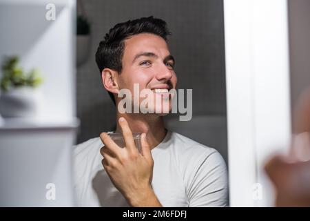 Ein Mann, der Parfüm benutzt, während er in den Spiegel schaut. Stockfoto