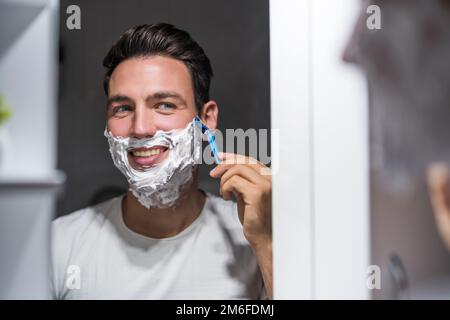 Ein Mann rasiert sich den Bart, während er sich in den Spiegel schaut. Stockfoto