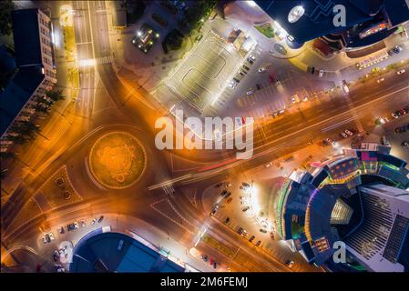 Luftdrohnenansicht der Nacht beleuchtete Innenstadt-Verkehrszirkel in der Nähe des Atrium-Gebäudes, Langzeitbelichtung Stockfoto