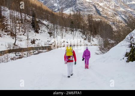 Mann und Frau mit einem Baby in einem Rucksackträger, die auf dem Feld in einer verschneiten Berglandschaft spazieren Stockfoto