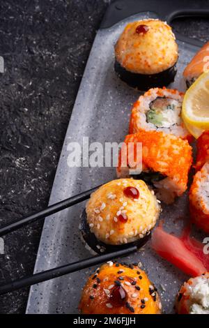Sushi-Rollenset serviert auf grauem Tablett am schwarzen Tisch. Flach verlegt. Schließen Stockfoto