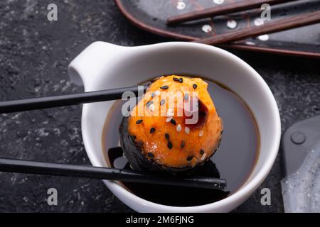 Gebackene Sushi-Brötchen, die unter Sojasoße gehalten werden. Sushi-Brötchen werden auf einem grauen Tablett serviert. Schließen Stockfoto