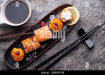Sushi-Rollenset serviert auf schwarzem Tablett am grauen Tisch. Flach verlegt. Stockfoto