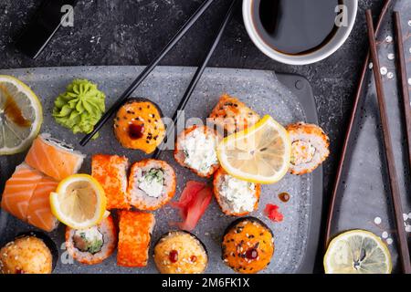 Sushi-Rollenset serviert auf grauem Tablett am schwarzen Tisch. Flach verlegt. Stockfoto