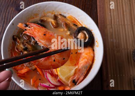 Miso Suppe mit Muscheln, Garnelen, Shiitake-Pilzen und Gemüse. Serviert an einem dunkelbraunen Holztisch. Flach verlegt Stockfoto