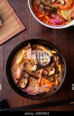 Miso Suppe mit Muscheln, Garnelen, Shiitake-Pilzen und Gemüse. Serviert an einem dunkelbraunen Holztisch. Flach verlegt Stockfoto