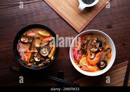 Miso Suppe mit Muscheln, Garnelen, Shiitake-Pilzen und Gemüse. Serviert an einem dunkelbraunen Holztisch. Flach verlegt Stockfoto