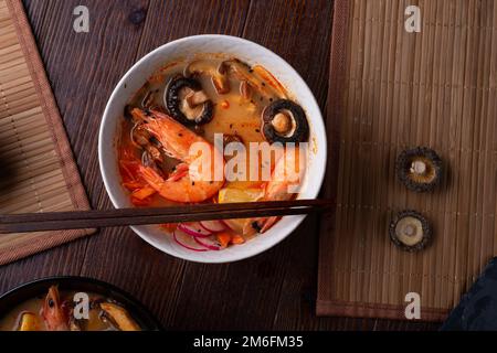 Miso Suppe mit Muscheln, Garnelen, Shiitake-Pilzen und Gemüse. Serviert an einem dunkelbraunen Holztisch. Flach verlegt Stockfoto