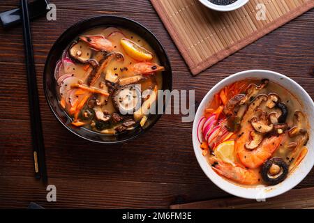 Miso Suppe mit Muscheln, Garnelen, Shiitake-Pilzen und Gemüse. Serviert in schwarz-weißen Schüsseln an einem dunkelbraunen Holztisch. fl Stockfoto