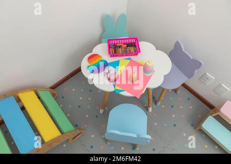 Draufsicht auf einen Kinderarbeitstisch in einer Kinderpraxis, mit Buntstiften, Zeichenblättern und Spielzeug. Stockfoto