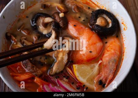 Miso Suppe mit Muscheln, Garnelen, Shiitake-Pilzen und Gemüse. Serviert an einem dunkelbraunen Holztisch. Flach verlegt Stockfoto