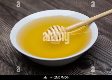 Honig mit Honig-Dipper in weißer Schüssel auf Holzhintergrund.Nahaufnahme Stockfoto