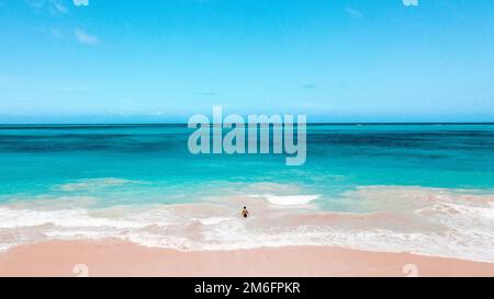 Ein atemberaubender Blick auf einen Mann, der von einem Strand in Hawaii in die schaumigen Wellen eines türkisfarbenen Meeres steigt Stockfoto