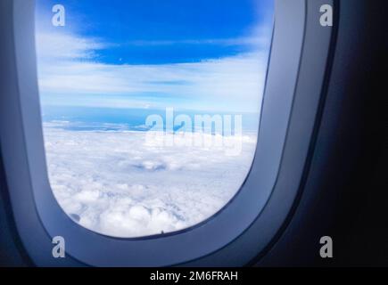 Der Blick aus dem runden Fenster des Flugzeugs auf die weißen Schneewolken, über die Wolken fliegen, das Konzept von Freiheit und Reisen Stockfoto