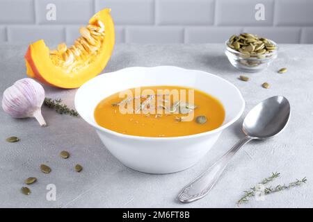 Kürbis-Püree-Suppe mit Kürbiskernen und Thymian auf einem weißen Teller und einem Stück reifem Kürbis. Gesunde Ernährung. Selektiver Fokus. Stockfoto